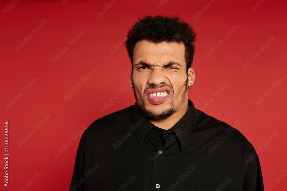 A handsome young man poses playfully with a silly expression in a vibrant studio. A handsome young man poses playfully with a silly expression in a vibrant studio.