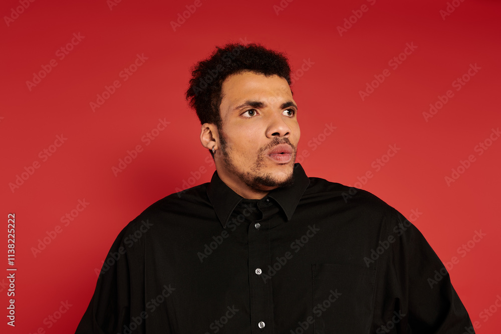 Handsome young man wearing a black shirt looks surprised against a vibrant red backdrop. Handsome young man wearing a black shirt looks surprised against a vibrant red backdrop.