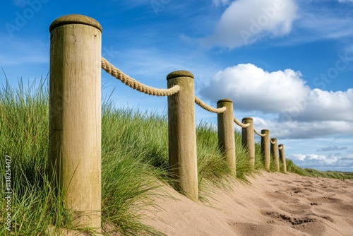 A beach fence made of weathered wooden posts and rope, with sand dunes and seagrass swaying in the breeze
