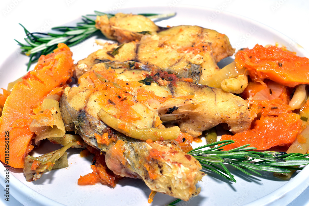 Cod fish with vegetables and herbs, ready to eat, lies on a plate, side view. Cod fish with vegetables and herbs, ready to eat, lies on a plate, side view.
