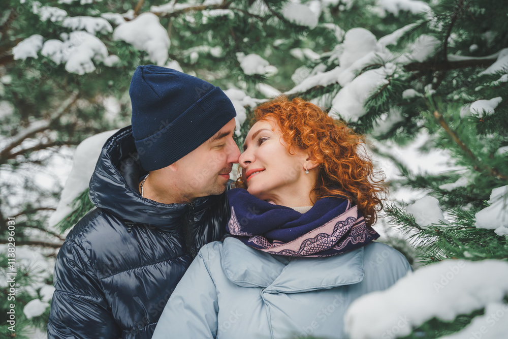 Fototapeta premium Love romantic love story. Happy couple of middle aged millennials, bright red-haired woman in winter snow park. Romantic date, kissing, hugging. Walking, having fun. Stylish blue clothes, jacket, hat