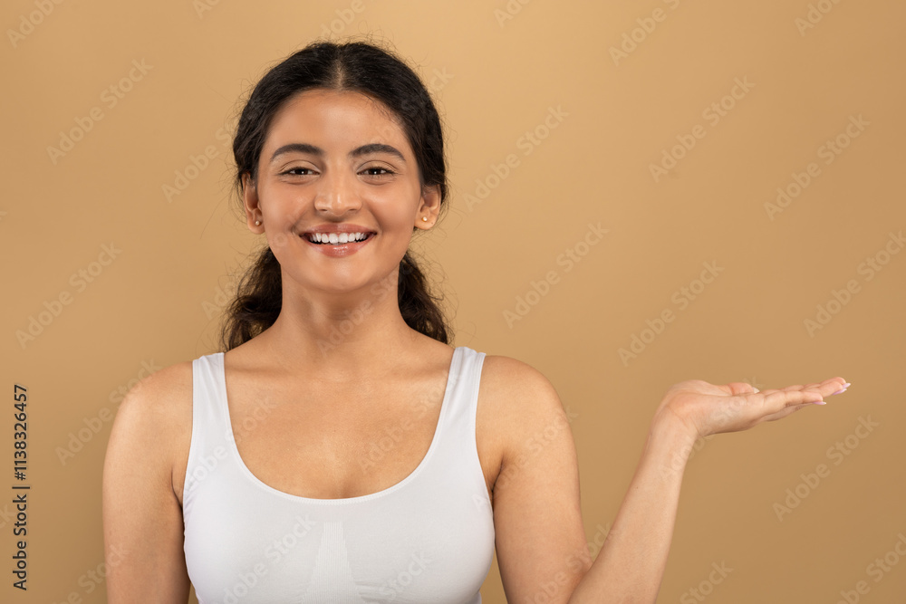 A young Indian woman with a radiant smile demonstrates her skincare routine, showcasing self-care in a relaxed indoor environment surrounded by earthy tones, copy space