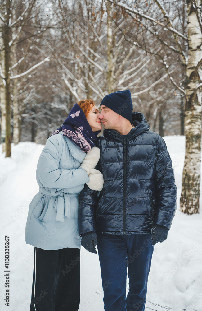 Love romantic love story. Happy couple of middle aged millennials, bright red-haired woman in winter snow park. Romantic date, kissing, hugging. Walking, having fun. Stylish blue clothes, jacket, hat Love romantic love story. Happy couple of middle aged millennials, bright red-haired woman in winter snow park. Romantic date, kissing, hugging. Walking, having fun. Stylish blue clothes, jacket, hat