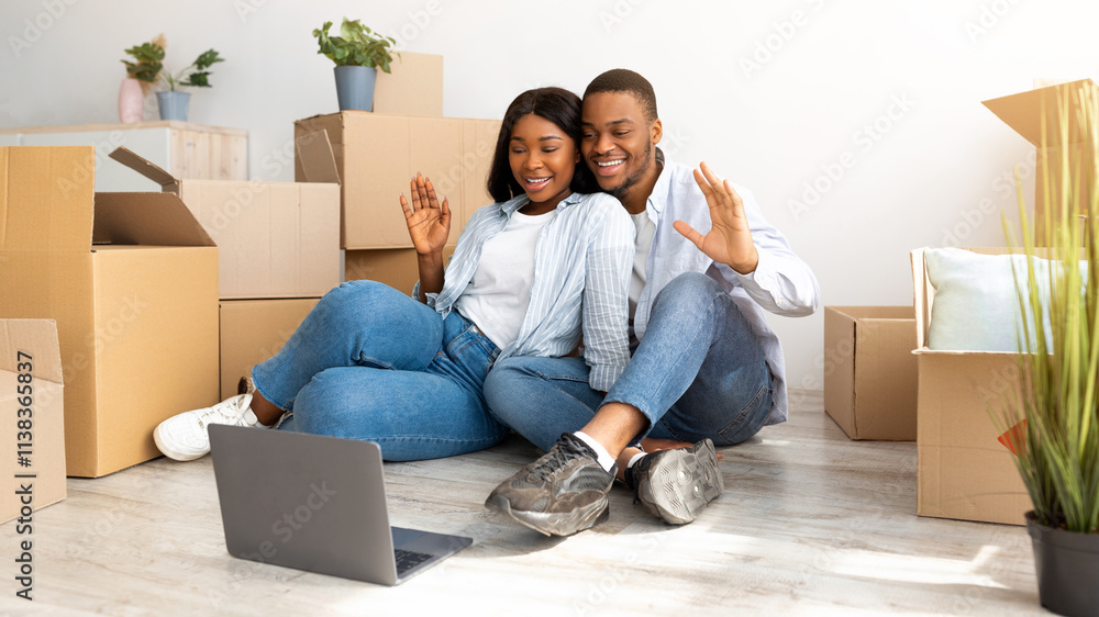 Loving black couple having video call with family on laptop computer and waving to camera, sitting on floor in their new home. Young newlyweds moving to their own apartment Loving black couple having video call with family on laptop computer and waving to camera, sitting on floor in their new home. Young newlyweds moving to their own apartment