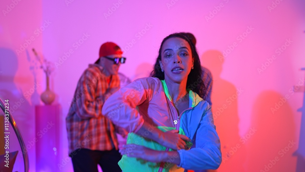 Attractive happy dancer looking at camera while smart woman moving at rhyme with neon light. Professional hispanic performer break dancing while wearing colorful cloth with diverse friend. Regalement. Attractive happy dancer looking at camera while smart woman moving at rhyme with neon light. Professional hispanic performer break dancing while wearing colorful cloth with diverse friend. Regalement.