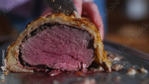 A person is cutting a piece of meat with a knife. The meat is cut in half and he is a roast photo