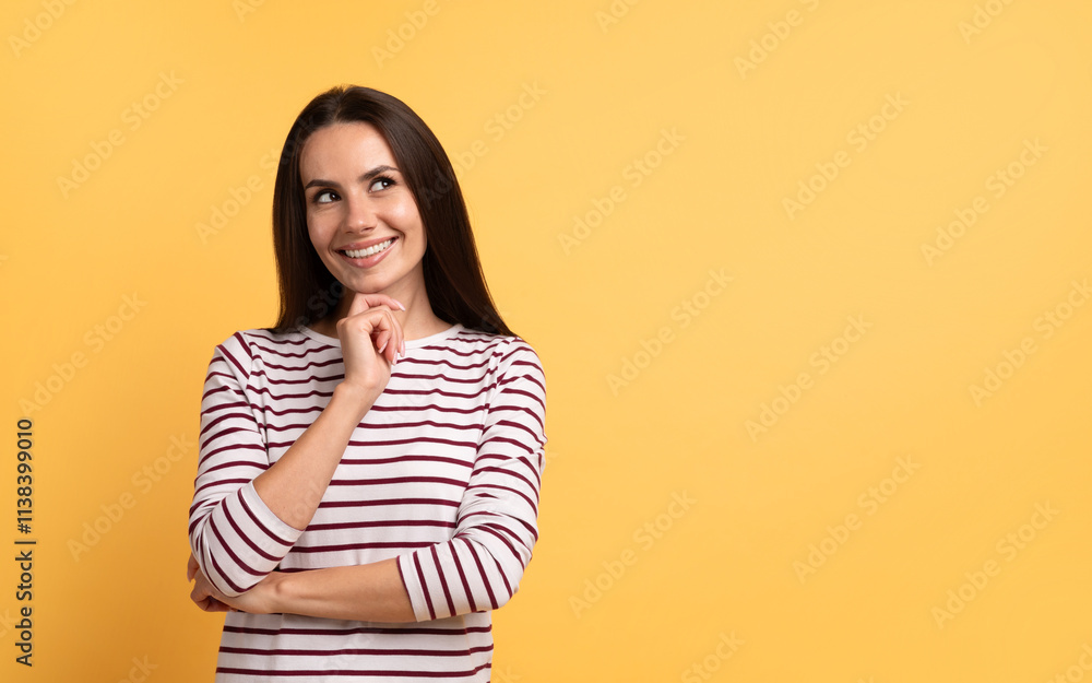 Positive young brunette woman looking at copy space, touching chin and smiling, isolated on yellow studio background Positive young brunette woman looking at copy space, touching chin and smiling, isolated on yellow studio background