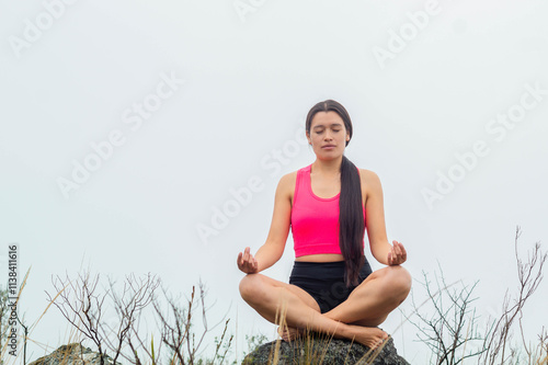 Mujer Delgada Sentada en una Roca Bajo el Cielo Nublado. Mujer delgada en top y short haciendo ejercicio en medio de un paisaje natural, perfecta representación de conexión con la naturaleza y cuidado photo