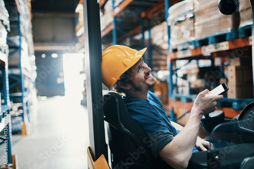 Male warehouse worker using smartphone near forklift photo