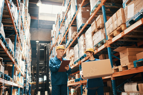 Warehouse workers in safety helmets managing inventory and carrying boxes in large storage facility