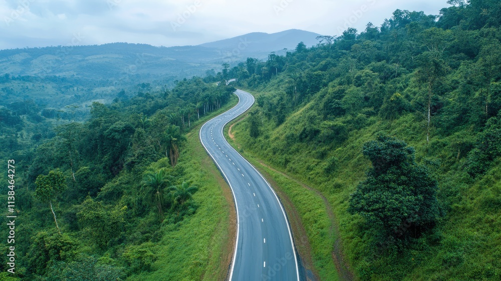 Fototapeta premium Curved scenic highway winding through lush green forested mountains under a cloudy sky