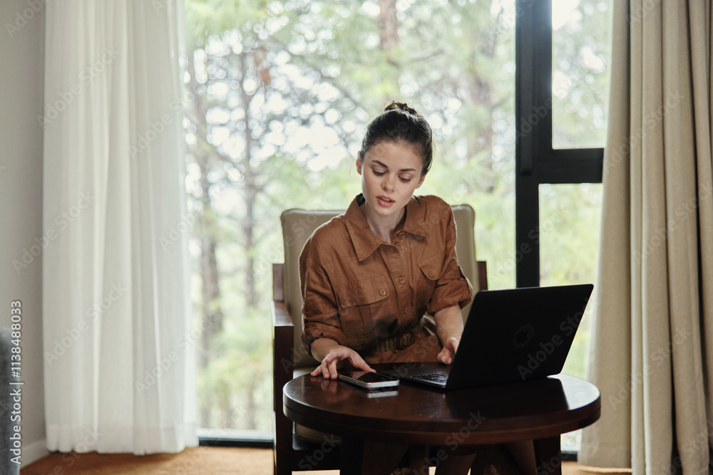 Young woman working on a laptop in a cozy indoor setting, showcasing a stylish brown outfit, focused on productivity amidst a serene natural backdrop Young woman working on a laptop in a cozy indoor setting, showcasing a stylish brown outfit, focused on productivity amidst a serene natural backdrop