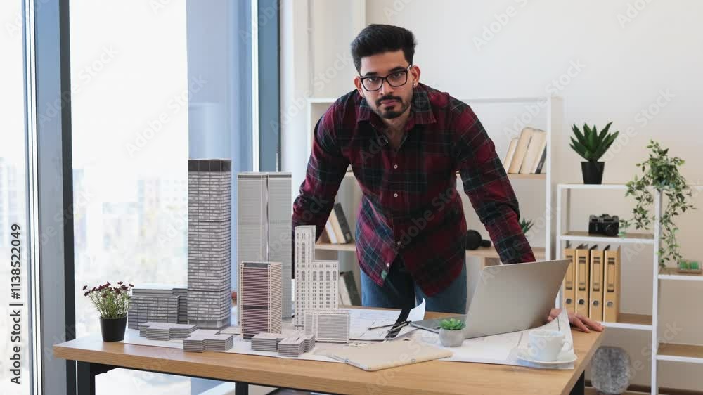 Indian male architect in 30s designing city architecture model at office desk with laptop and buildings. Creative professional working on urban development project in modern workspace. Indian male architect in 30s designing city architecture model at office desk with laptop and buildings. Creative professional working on urban development project in modern workspace.