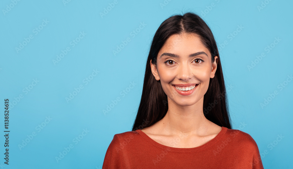 A woman with long brunette hair smiles brightly, showcasing her joyful demeanor. She stands in front of a vibrant blue background, copy space, closeup A woman with long brunette hair smiles brightly, showcasing her joyful demeanor. She stands in front of a vibrant blue background, copy space, closeup