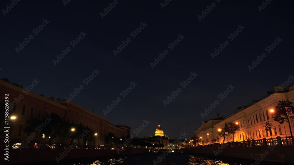Boat tour along Moyka River past historical buildings with the dome of St Isaac's Cathedral in the distance at night, Saint-Petersburg, Russia Boat tour along Moyka River past historical buildings with the dome of St Isaac's Cathedral in the distance at night, Saint-Petersburg, Russia