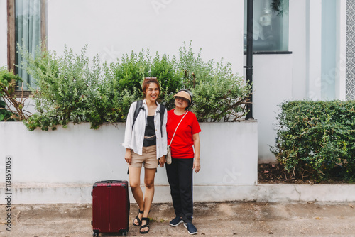 Asian Thai old mom and young adult daughter carry backpack, women walking with luggage on the street, standing in front of building, happy traveling together. photo