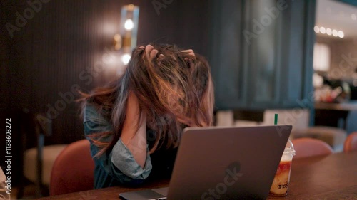 Frustrated and Overwhelmed. A young woman runs her hands through her hair, overwhelmed by the pressures of work, staring at her laptop in a moment of frustration.  