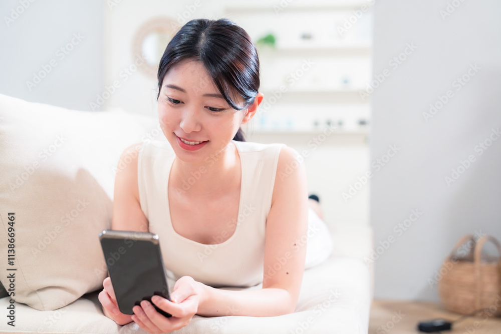 ソファで寝転がってスマホを使う若い女性 ソファで寝転がってスマホを使う若い女性
