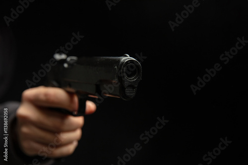 Hand holding a gun closeup, armed man on dark background. Danger and crime photo