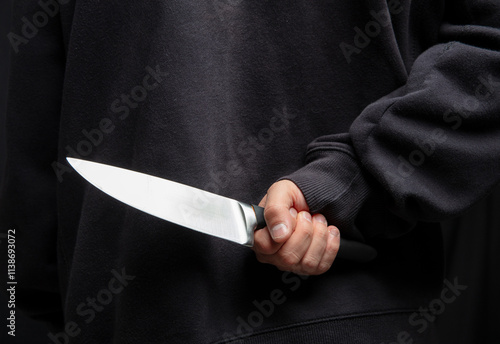 Фотография Robber hiding a knife behind his back, man holding a weapon in hand closeup