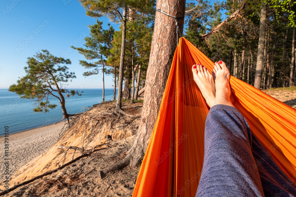 Part of the woman's legs in a hammock with view on a forest and a lake