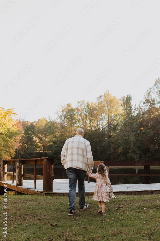 Fototapeta premium Father and Daughter Walking Hand-in-Hand by a Rustic Dock in Autumn – Heartwarming Family Moment, Scenic Nature Background, Bonding Time, Peaceful Outdoor Setting, Warm Light Capturing Parent-Child