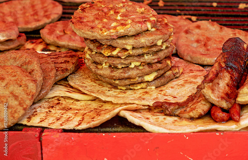 Pile of grilled beef burgers with cheese on top in agricultural fair market stall