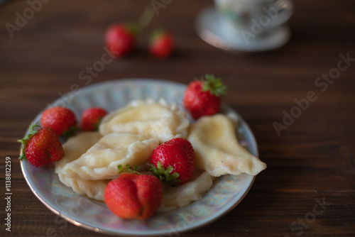 A close-up of a plate of homemade dumplings with fresh strawberries, lightly dusted with powdered sugar, placed on a dark wooden table. The warm tones create an inviting and cozy atmosphere.