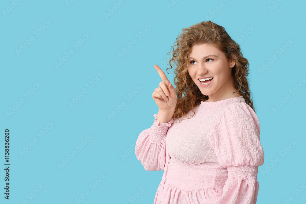 Beautiful young happy Muslim woman pointing at something on blue background
