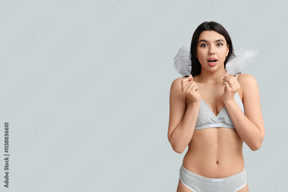 Fototapeta premium Shocked young woman with soft feathers on grey background. Epilation concept