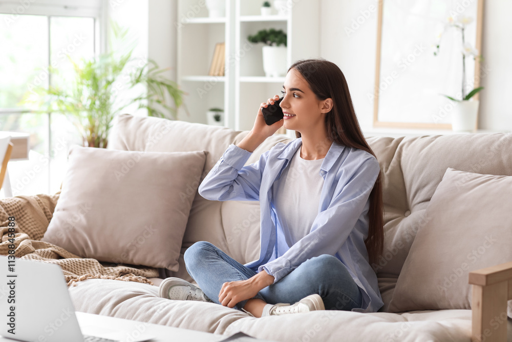 Beautiful young happy woman with laptop talking by mobile phone on sofa at home Beautiful young happy woman with laptop talking by mobile phone on sofa at home