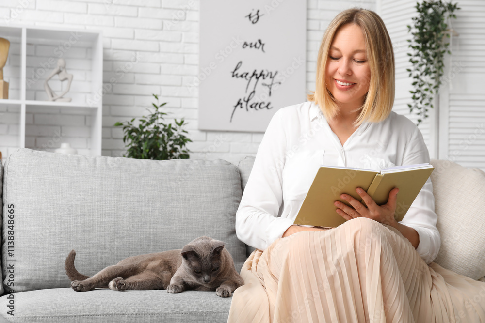 Middle-aged woman reading book with cute cat on sofa at home