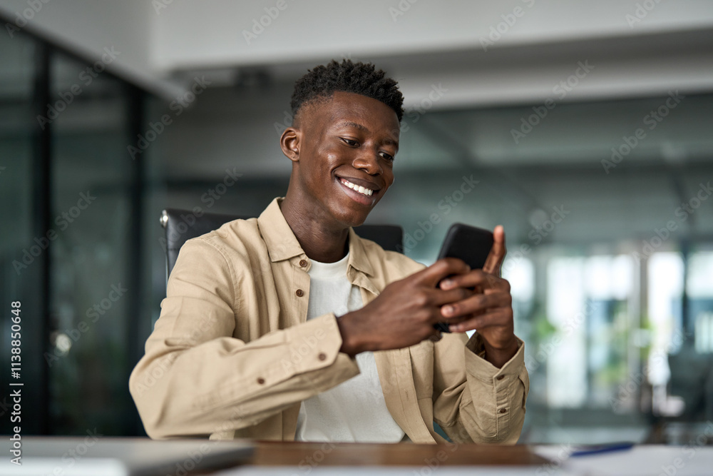Happy busy Black business man employee using cellphone at work. Smiling young adult African male worker holding mobile phone smart technology gadget in hands working in office sitting at desk. Happy busy Black business man employee using cellphone at work. Smiling young adult African male worker holding mobile phone smart technology gadget in hands working in office sitting at desk.