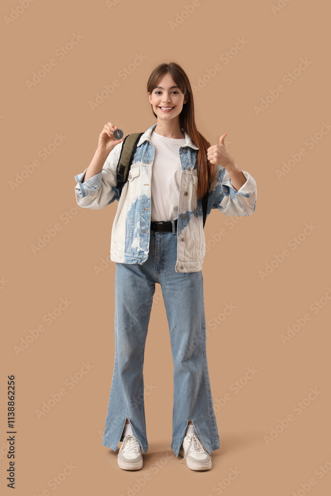 Female tourist with compass and backpack showing thumb-up on beige background Female tourist with compass and backpack showing thumb-up on beige background