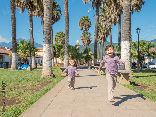 Beautiful girls run around happily in the middle of a square full of vegetation and surrounded by colonial architecture. photo