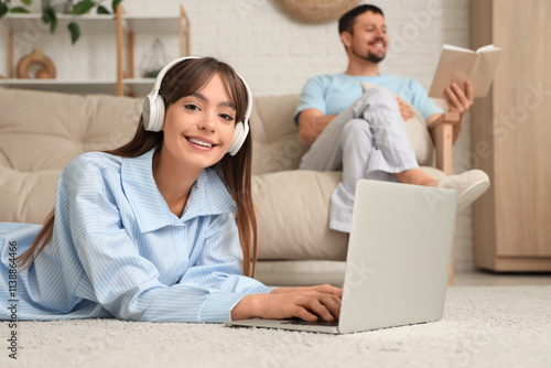 Young happy woman in pajamas with laptop and his boyfriend reading book at home