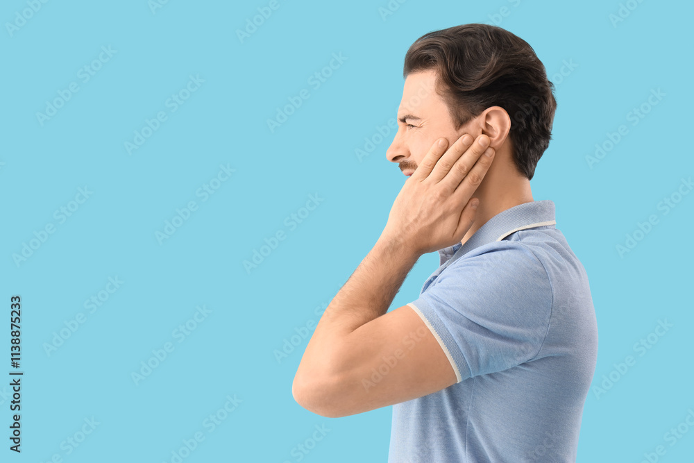 Young man suffering from ear pain on blue background Young man suffering from ear pain on blue background
