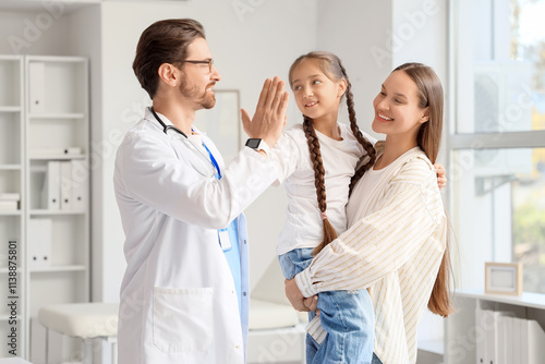 Male pediatrician giving high-five to girl and mother in clinic photo