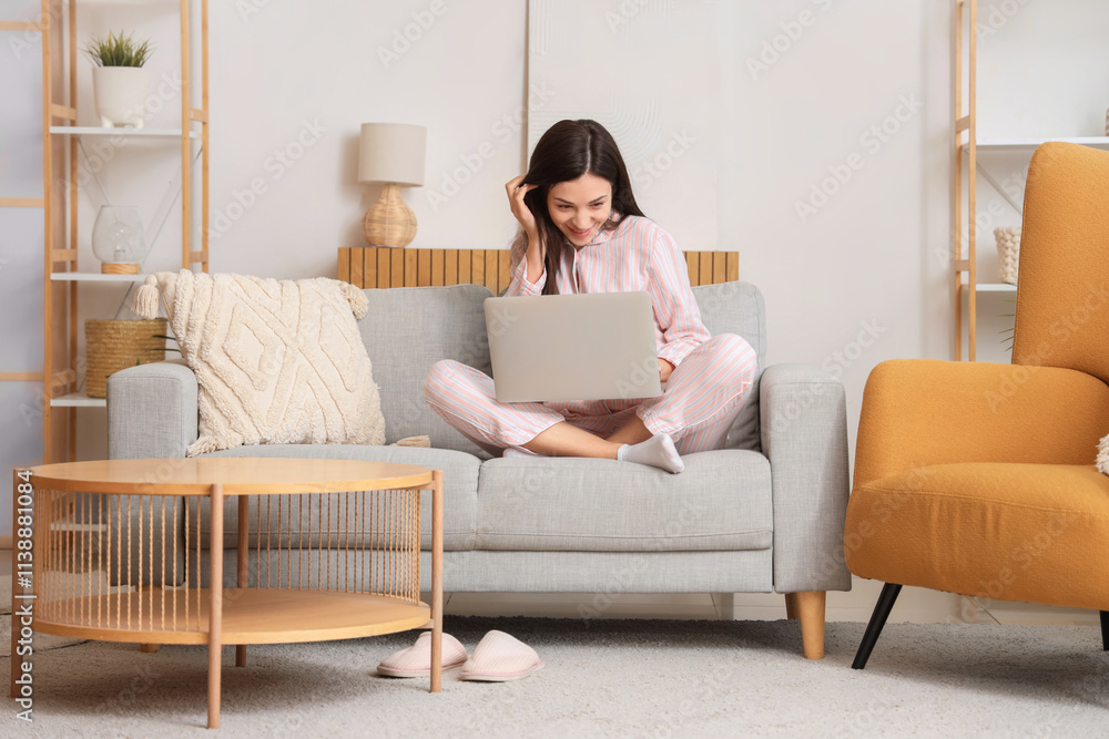 Young woman in striped pajamas working with laptop on sofa at home Young woman in striped pajamas working with laptop on sofa at home