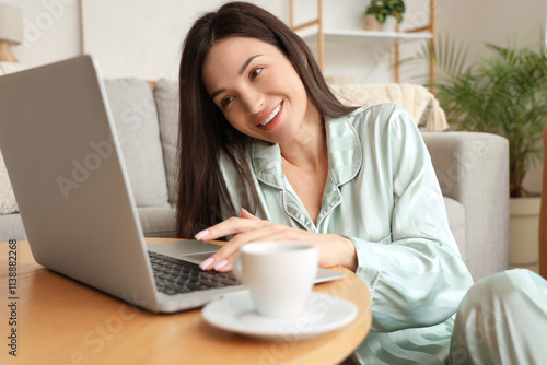 Young woman in green pajamas working with laptop on table at home