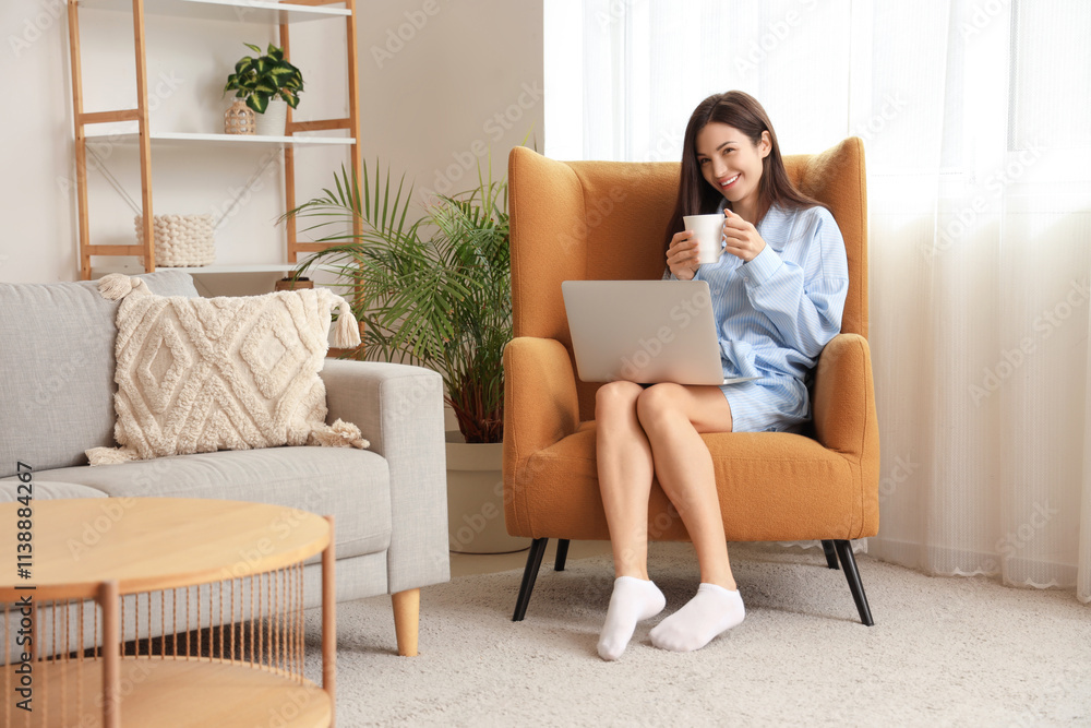 Young woman in blue pajamas with coffee and laptop working on armchair at home Young woman in blue pajamas with coffee and laptop working on armchair at home