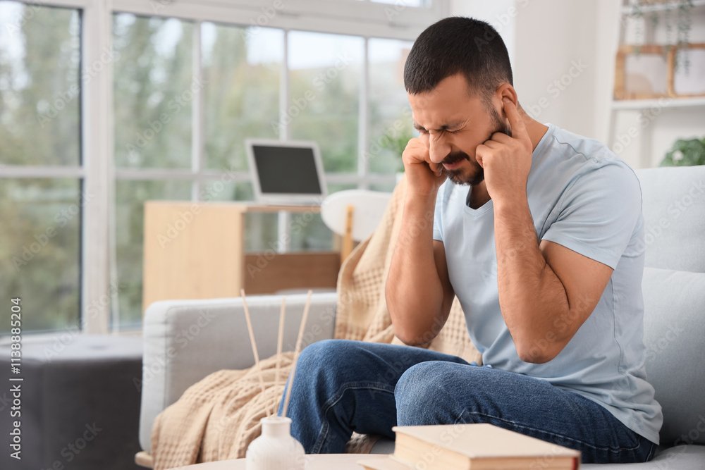 Young man with hearing problem covering his ears on sofa at home Young man with hearing problem covering his ears on sofa at home