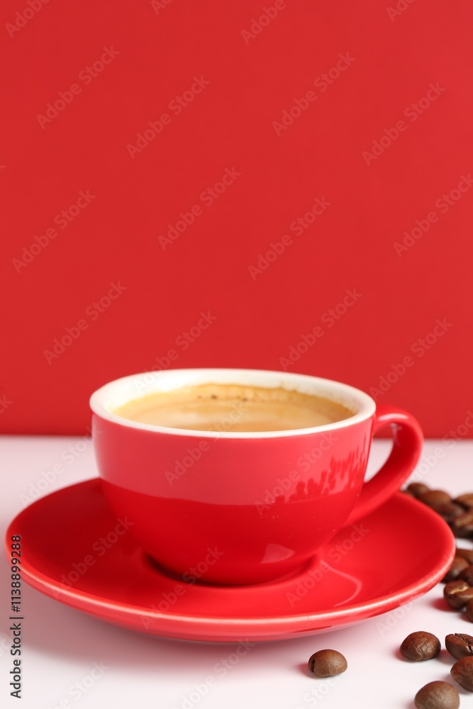 Red cup with coffee and roasted beans on white table, space for text Red cup with coffee and roasted beans on white table, space for text