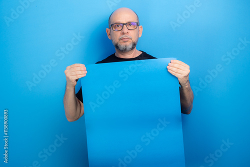 Bearded, bald man wearing prescription glasses and a black shirt holding a blue poster. Confident and focused. photo