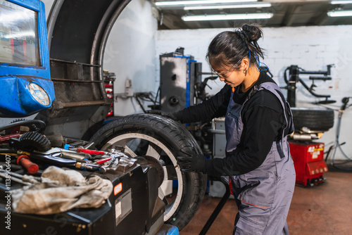 Female chinese mechanic mounting tire on wheel in auto repair shop