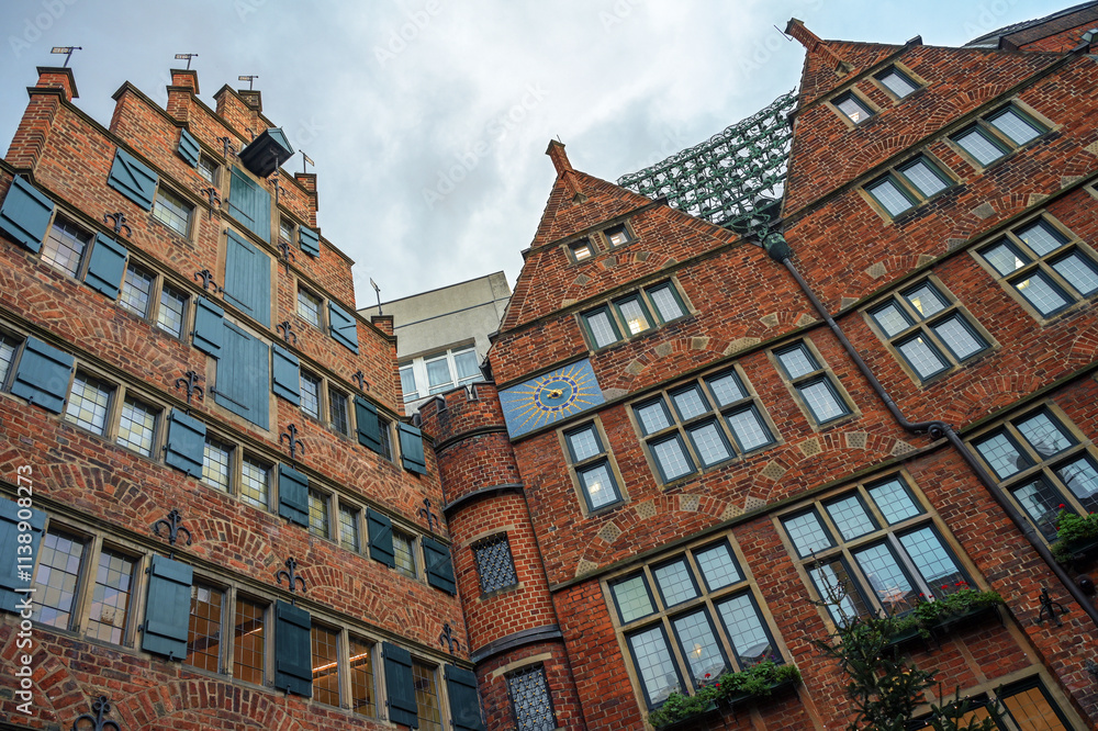 Fototapeta premium Historic buildings in red brick architecture in Boettcherstrasse in Bremen, Germany with the celebrated carillon or glockenspiel between the gables under a cloudy sky