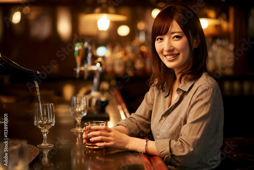 Naklejka バーのカウンターでウイスキーを飲む笑顔の女性