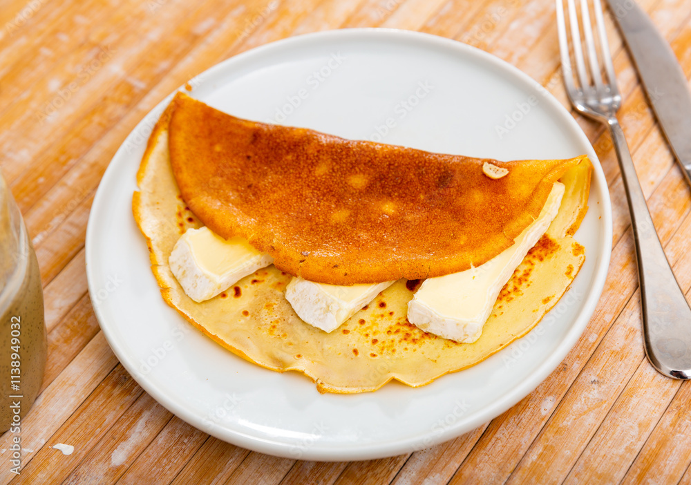 On plate are several rolled delicate pancakes with ruddy edge and bars of cream brie cheese. Hearty snack is complemented by cup of fragrant coffee, tea On plate are several rolled delicate pancakes with ruddy edge and bars of cream brie cheese. Hearty snack is complemented by cup of fragrant coffee, tea
