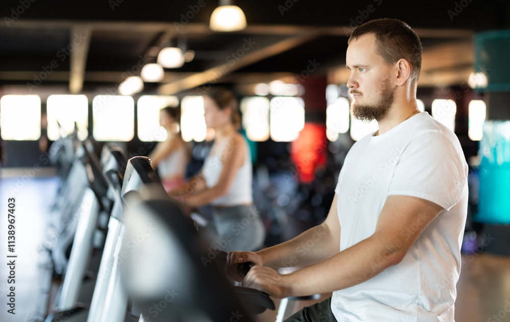 Young athletic man in sportswear training on exercise bike in gym Young athletic man in sportswear training on exercise bike in gym