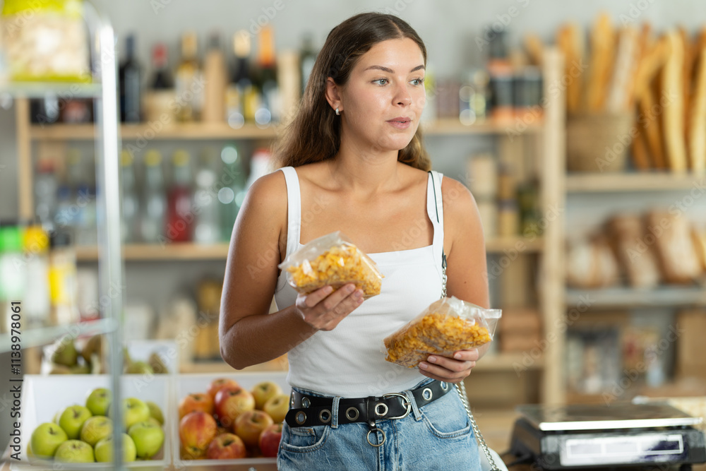 Young female shopper chooses corn flakes in package in grocery store